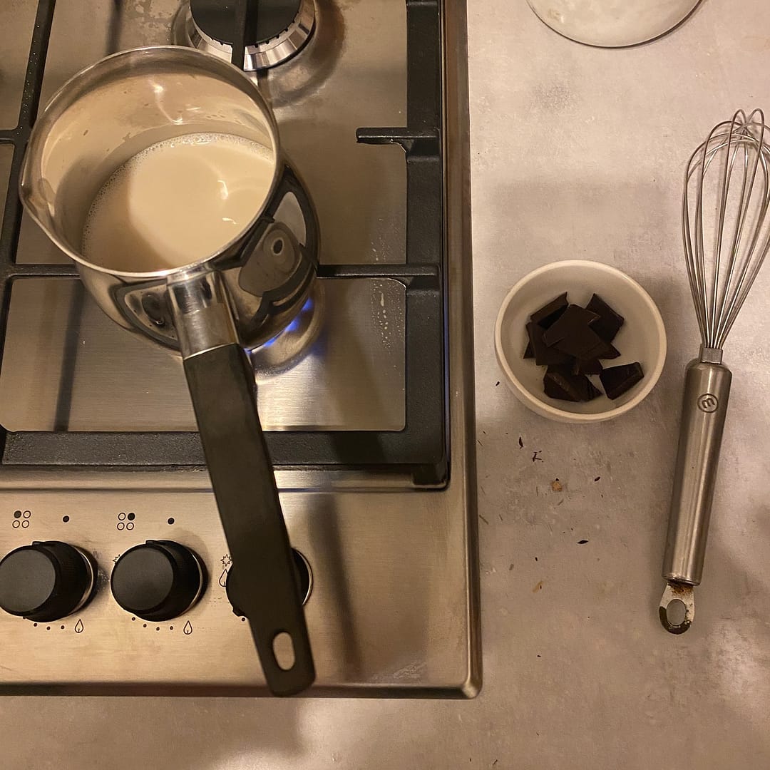 milk simmering on the hob with pieces of chocolate in a bowl and a whisk beside