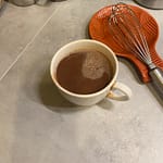 hot chocolate in a cup with a whisk and red spoon rest nearby